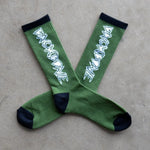 Backbone Crew Socks: buttery soft green crew socks with black toes, heels, and cuffs. Each sock features "BACKBONE" in bold white lettering on the mid-shin. Shown laid out on a gray surface.