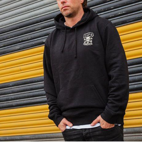 Against a yellow and gray striped backdrop, someone in a groovy BSD More Speed Hoodie exudes an effortlessly cool vibe.