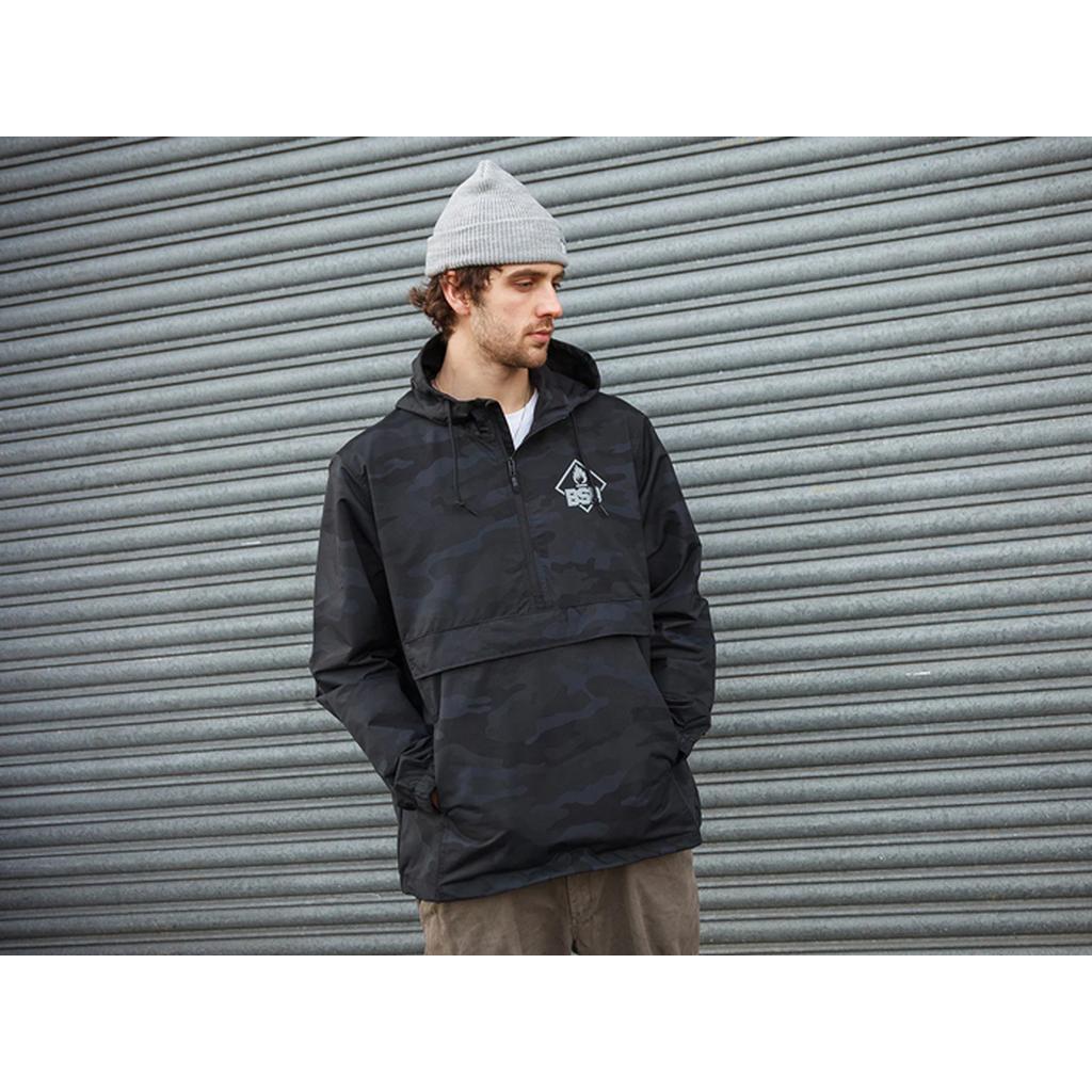 A man in a BSD Roastin Jacket and gray beanie stands before a corrugated metal wall, gazing to the side.