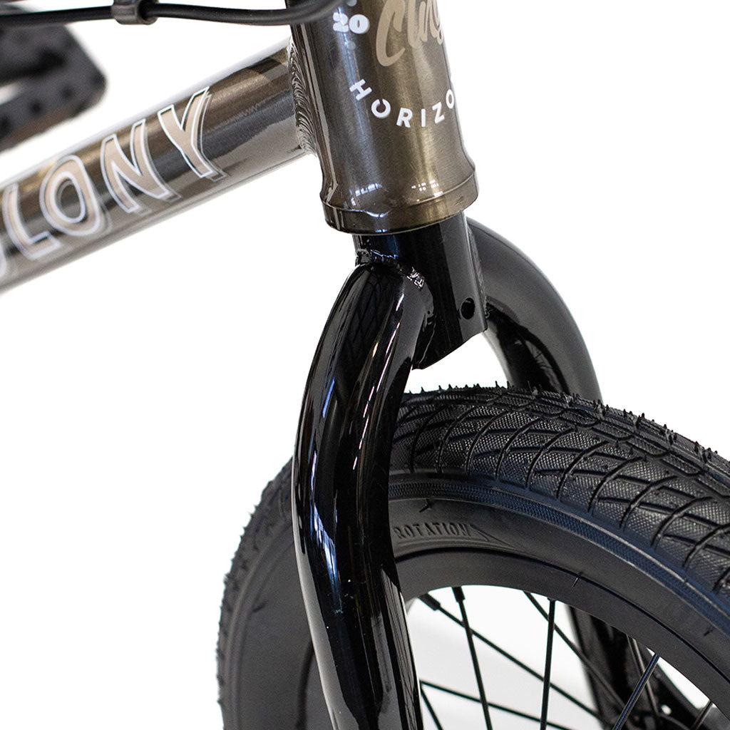 Close-up of the front fork and tire of a BMX bike, showcasing the brand "Colony" and model "Horizon" on the frame. The product is the Colony Horizon 12 Inch Bike. The tire displays a textured tread, while the fork has a glossy black finish, all complemented by a lightweight alloy frame designed for superior performance.