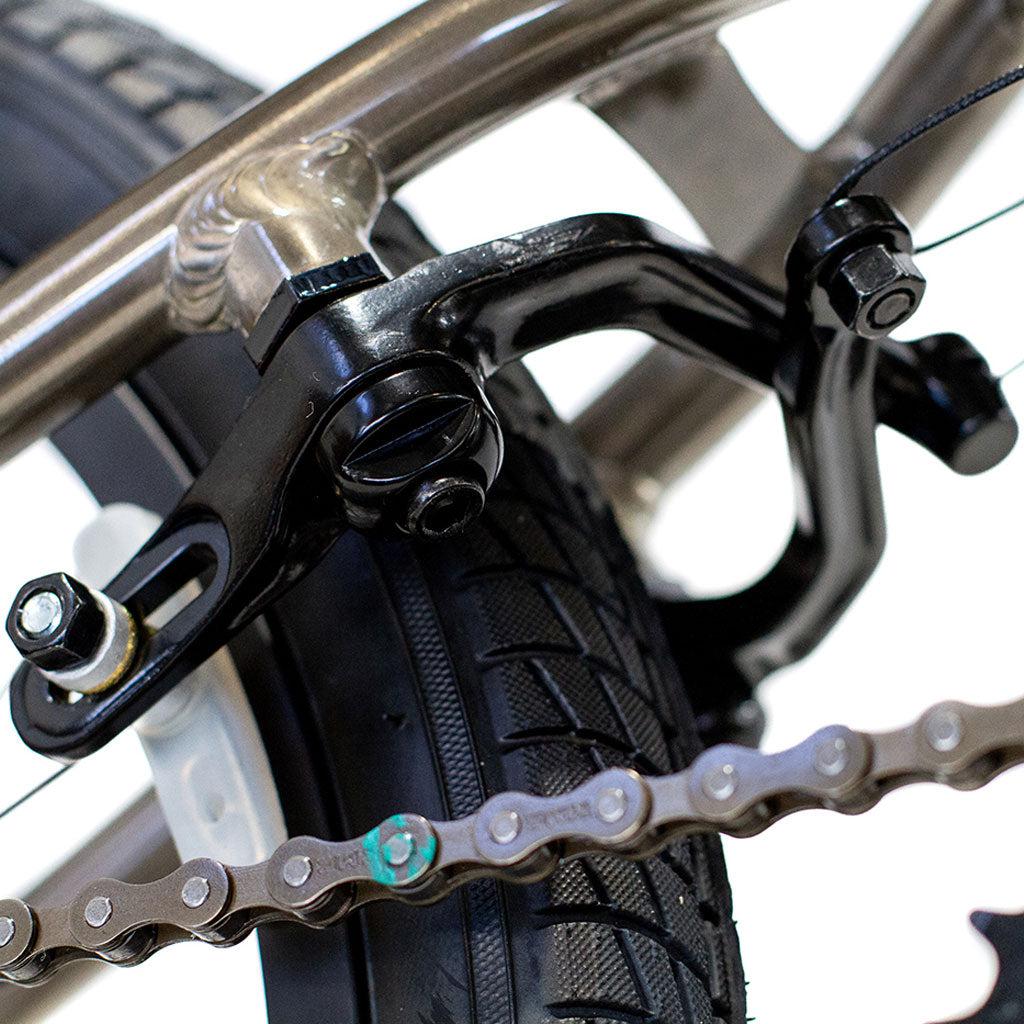 Close-up of the Colony Horizon 20 Inch Bike’s rear tire, chain, and black caliper brake against a neutral background, showcasing its lightweight alloy frame.