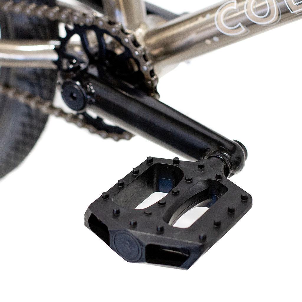 Close-up of a black metal pedal and crank arm on the Colony Horizon 20 Inch Bike, with its lightweight alloy frame and chainring visible in the background.