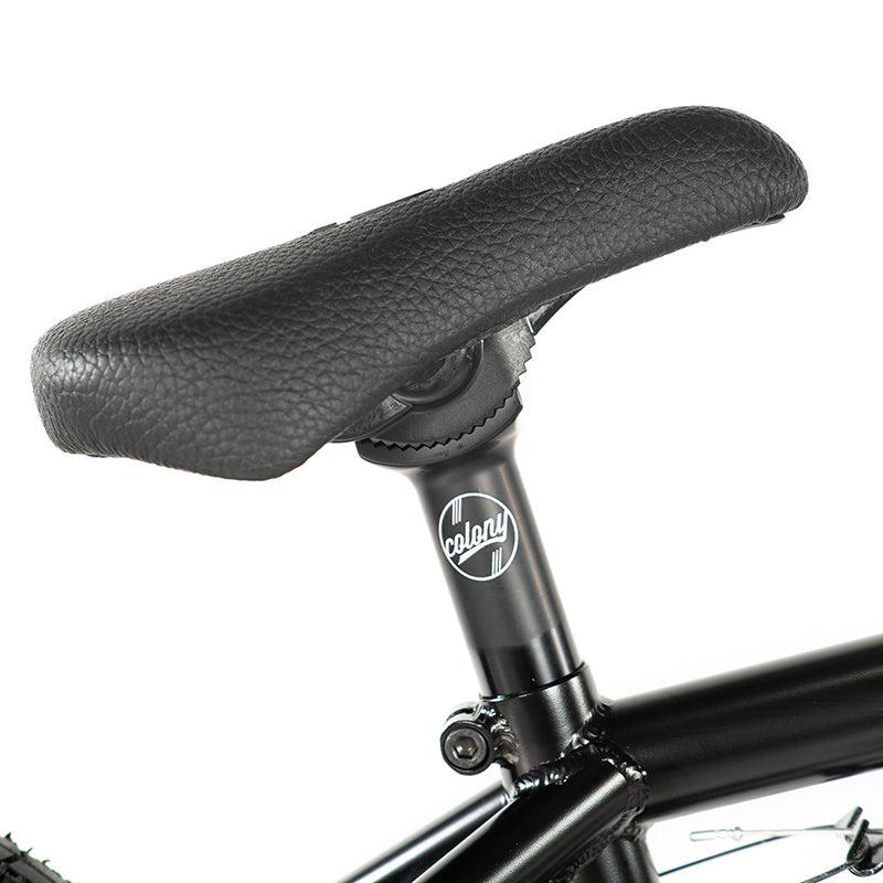 Close-up of a black textured bicycle seat with the Colony BMX logo on the seat post, enhancing both comfort and style for your Colony Sweet Tooth Pro Elite 18 Inch BMX Bike rides.