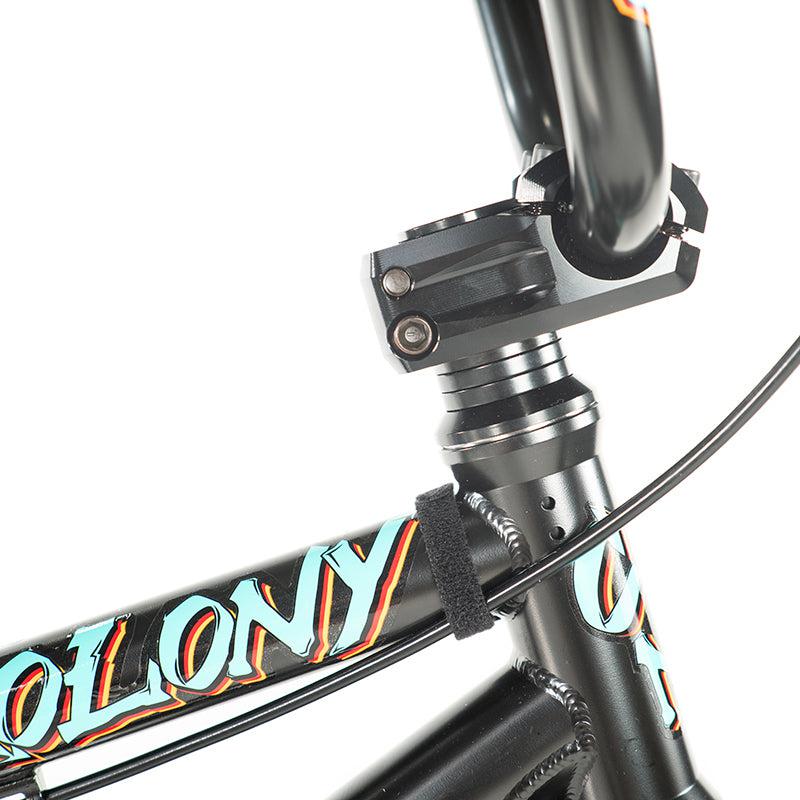 Close-up of a black Colony Sweet Tooth Pro Elite 18-Inch BMX bike frame with a colorful "Colony BMX" decal, displaying handlebars, stem, and part of the front fork.