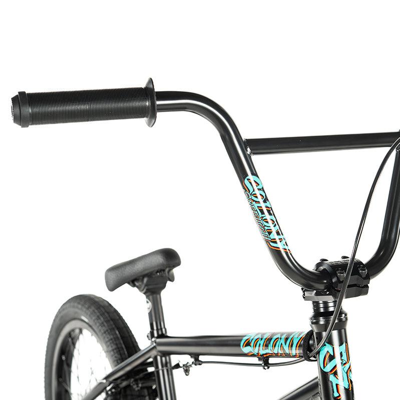 Close-up of a Colony Sweet Tooth Pro Elite 18 Inch BMX bike, displaying its black frame with teal and white decals, highlighting the handlebars, grips, and seat.