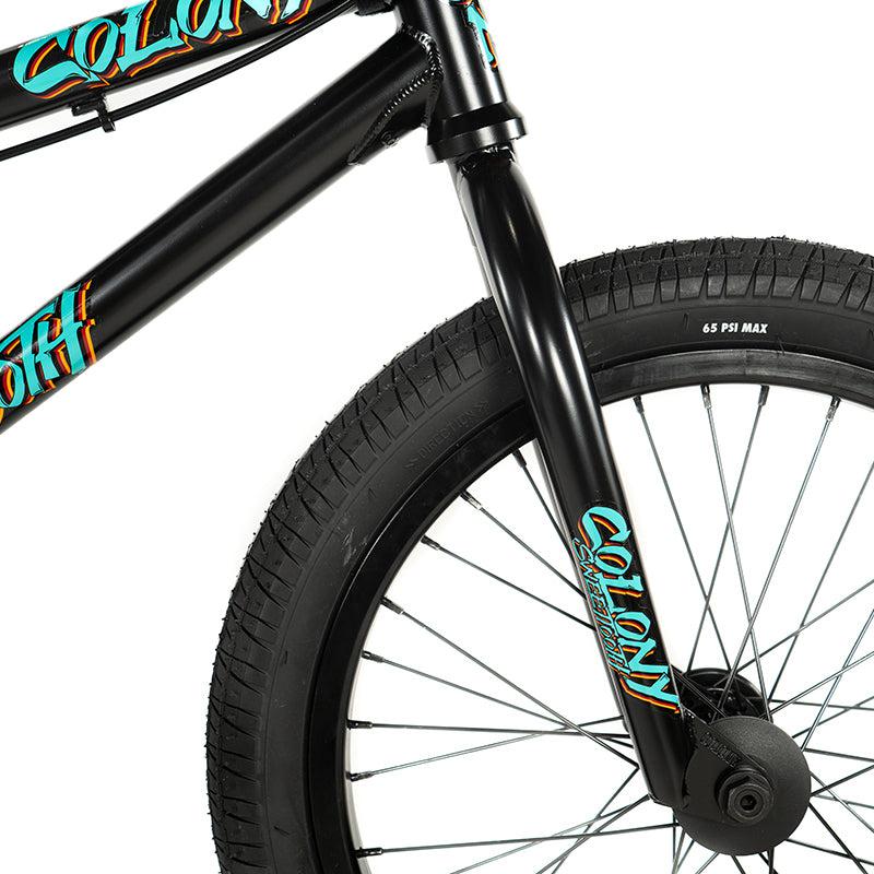Close-up of a Colony Sweet Tooth Pro Elite 18 Inch BMX bike in black, highlighting the front wheel and fork, featuring the iconic Colony BMX logo and a tire rated at 65 PSI max.