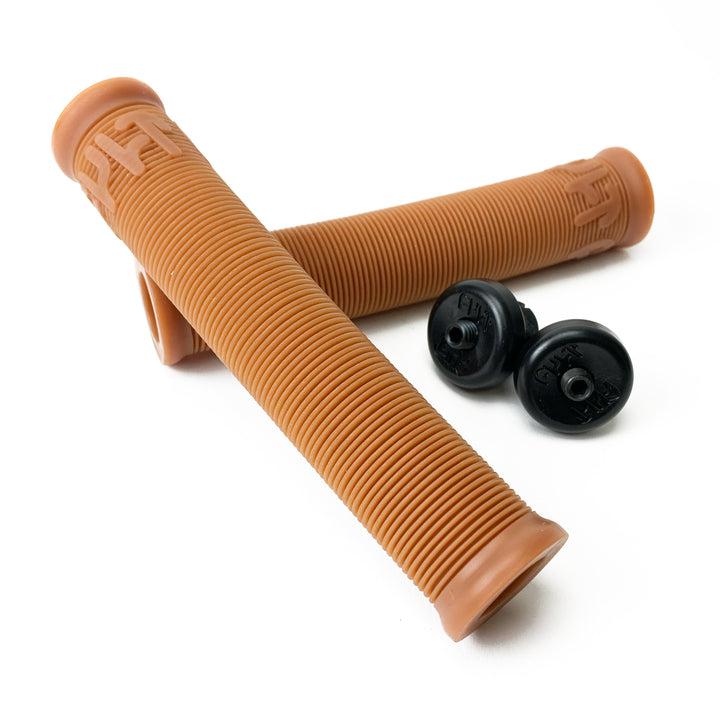 A pair of Cult Crew Grips featuring a brown BMX ribbed design, accompanied by two black end plugs, rests on a white background. They are crafted from durable rubber for long-lasting performance.