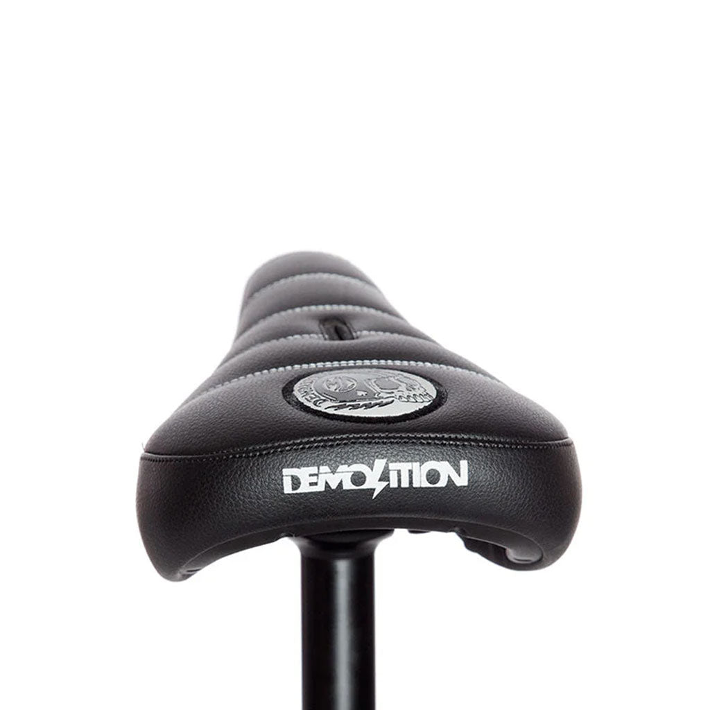 Close-up of a black Demolition Matt Cordova Seat (V2) with "Demolition" branding and logo on top, featuring Pivotal Fat Cap Padding for enhanced comfort and durability.