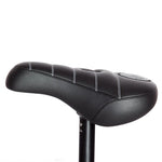 Close-up of the black Demolition Matt Cordova Seat (V2), showcasing its leatherette materials and white stitching, mounted on a black seat post with Pivotal Fat Cap Padding.