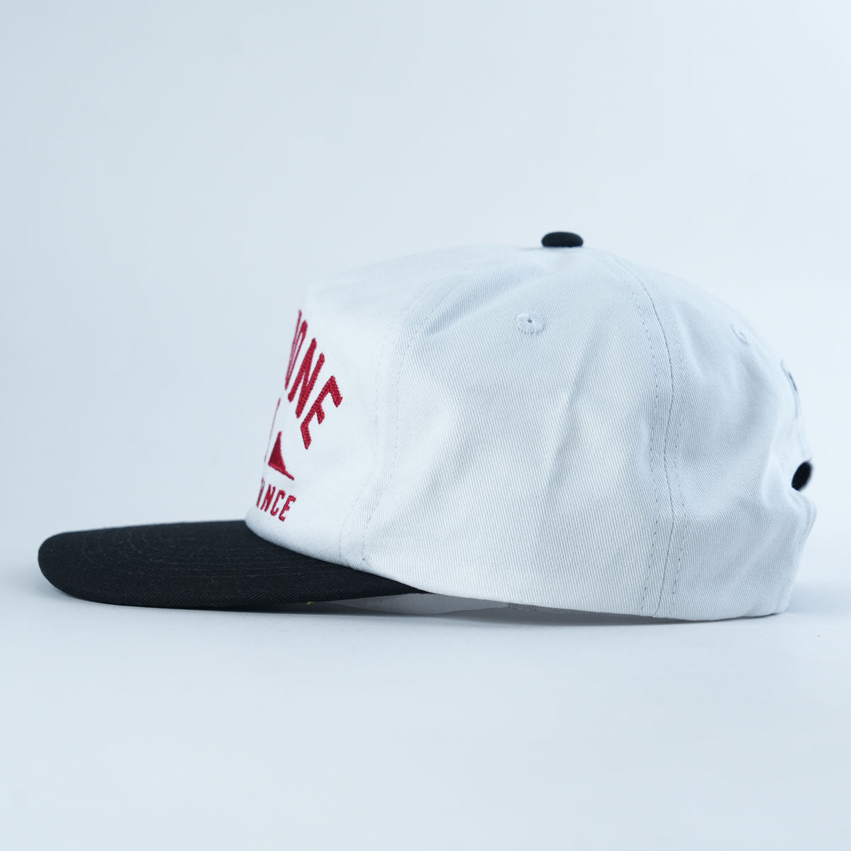 Backbone Distance Snapback Hat: An unstructured white 5-panel cap featuring a black brim, red embroidered text, and black ventilation eyelets, displayed from the right side against a plain white background.