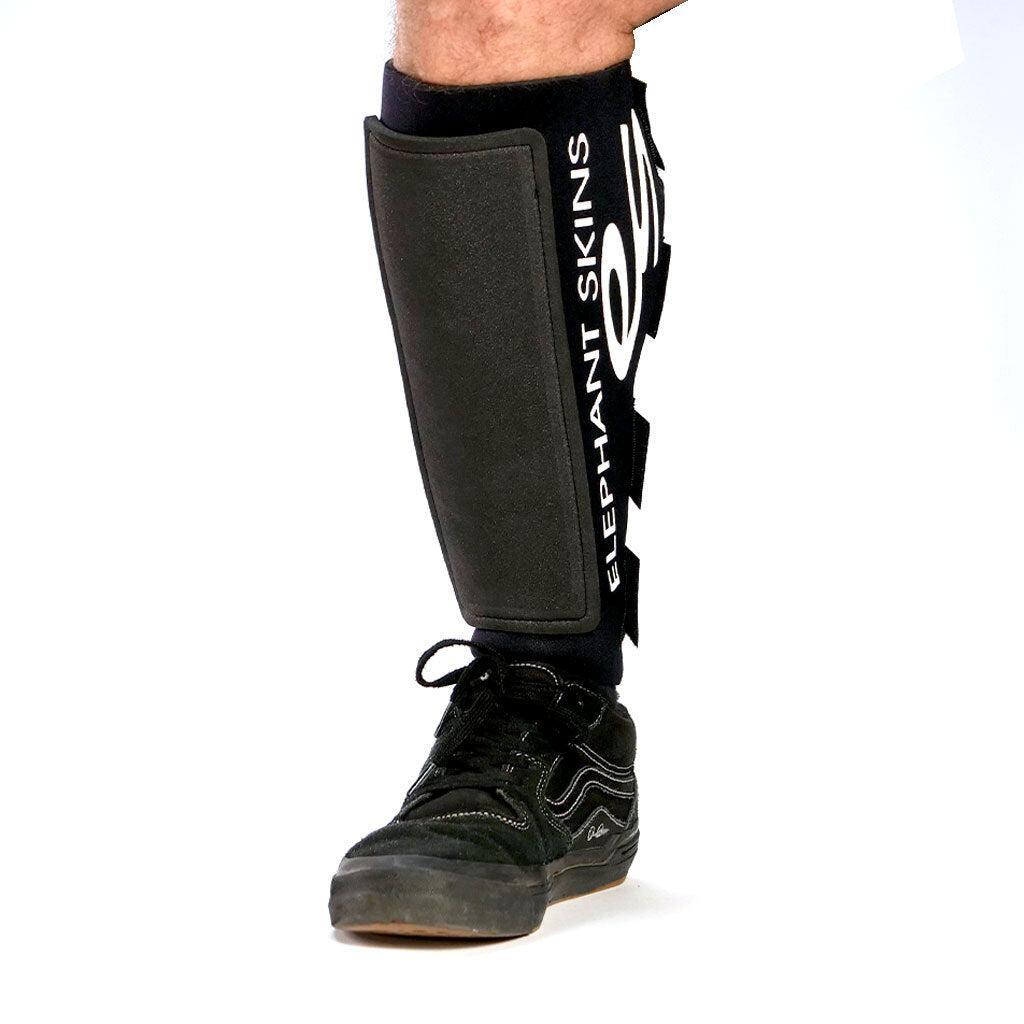 A person wearing black Elephant Skins Shin Pads, noted for lightweight protection, on their lower leg and paired with a black sneaker, set against a white background.