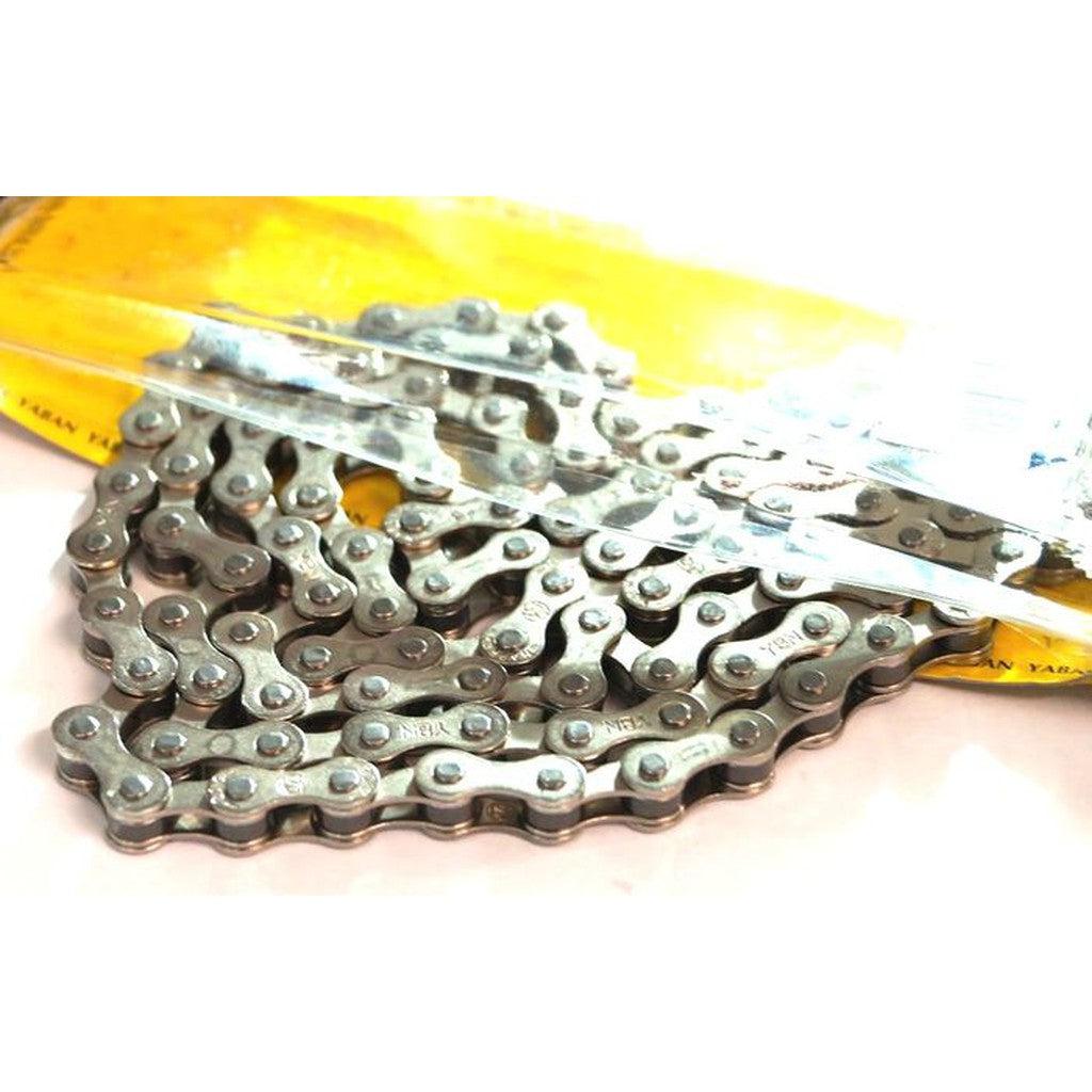A YBN Freestyle chain 1/2-1/8 with colored outer plates is partially removed from its yellow packaging and displayed on a white surface, ideal for single-speed setups.