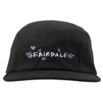 The Fairdale Nora V Camper Cap is a black five-panel hat featuring custom Nora bike-inspired artwork with "FAIRDALE" embroidered in white and purple, surrounded by small purple hearts and leaves.
