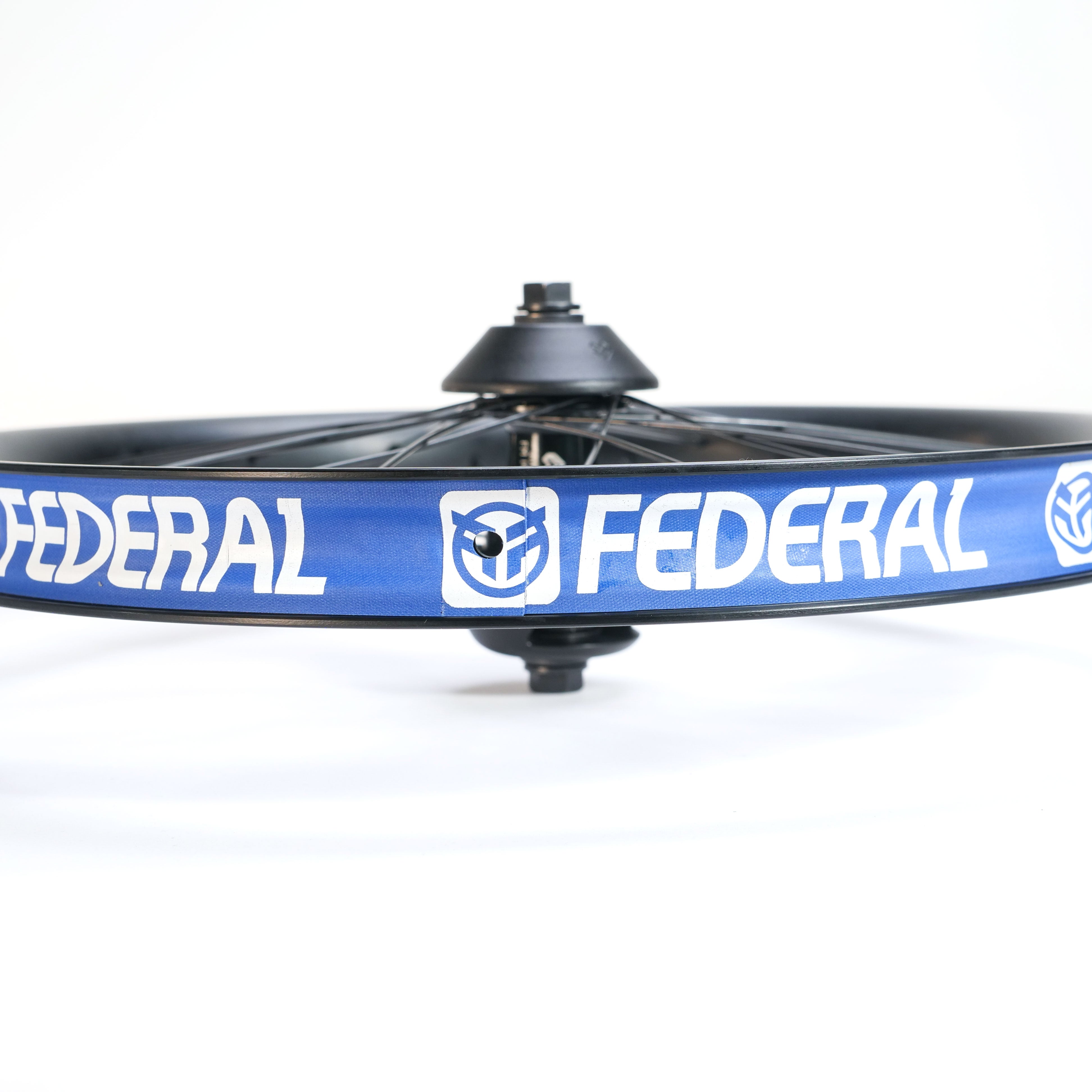 Close-up of the black Federal X Eclat FM Shift Hybrid Custom Wheel with a blue rim displaying the white "FEDERAL" logo and icon, set against a white background.