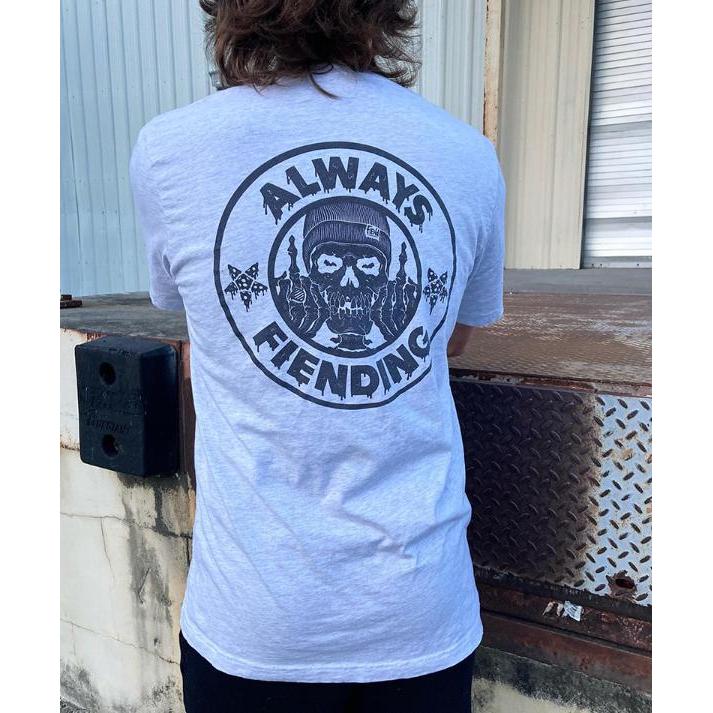 A person in a gray Fiend Always Fiending Shirt (Ash) stands near a metal platform, showcasing the style made popular by Garrett Reynolds' designs.