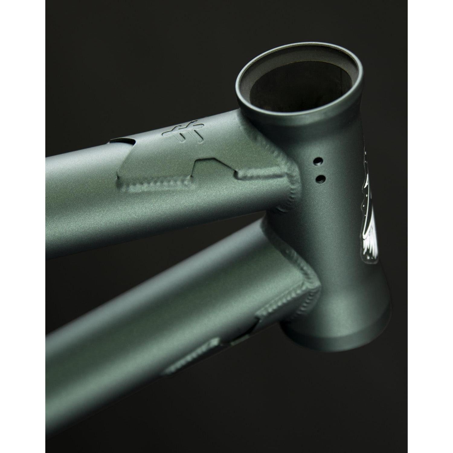 Close-up of a matte green Fly Bikes Aire Frame, highlighting the head tube and welds against a dark background.
