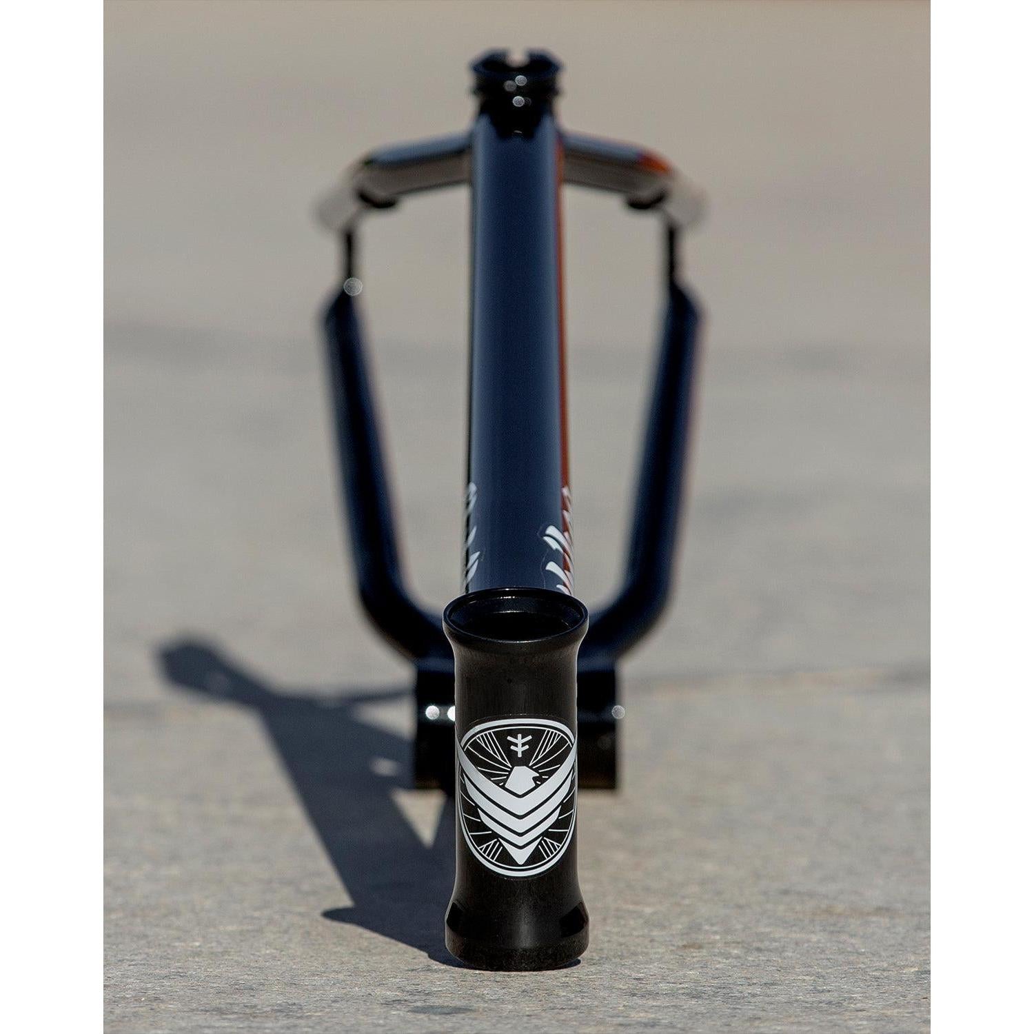 Close-up of a black Fly Bikes Dove 13.2 Frame (Josh Dove Signature) bicycle on concrete, highlighting the geometric logo at the front—ideal for transition riding adventures.