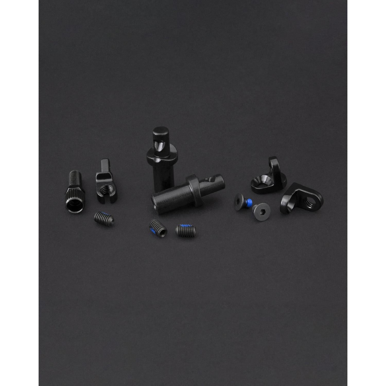 The Fly Bikes EBS Brake Mount Kit features small black mechanical components, including screws, nuts, and cylindrical parts, arranged on a dark surface—essential for any project.
