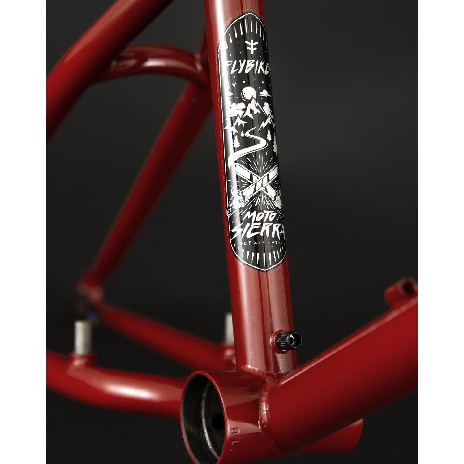 Close-up of the red Fly Bikes Motosierra Frame highlighting a black and white decal with design elements, featuring "Flybike" and "Moto Sierra" text, plus welded chainstay brake mounts for trails-specific geometry.