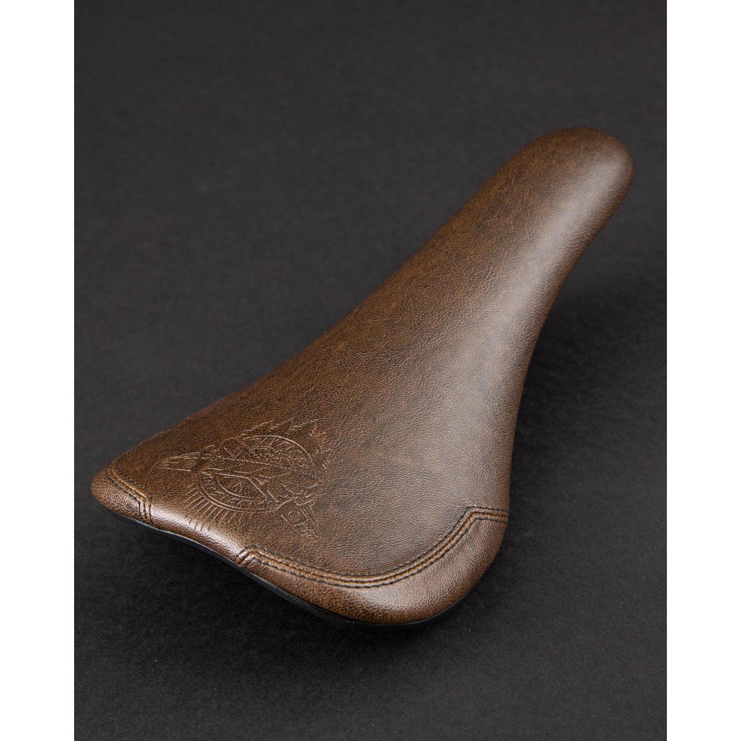 Fly Bikes Motosierra Railed Seat features a brown synthetic leather design with stitched details, set against a dark background.