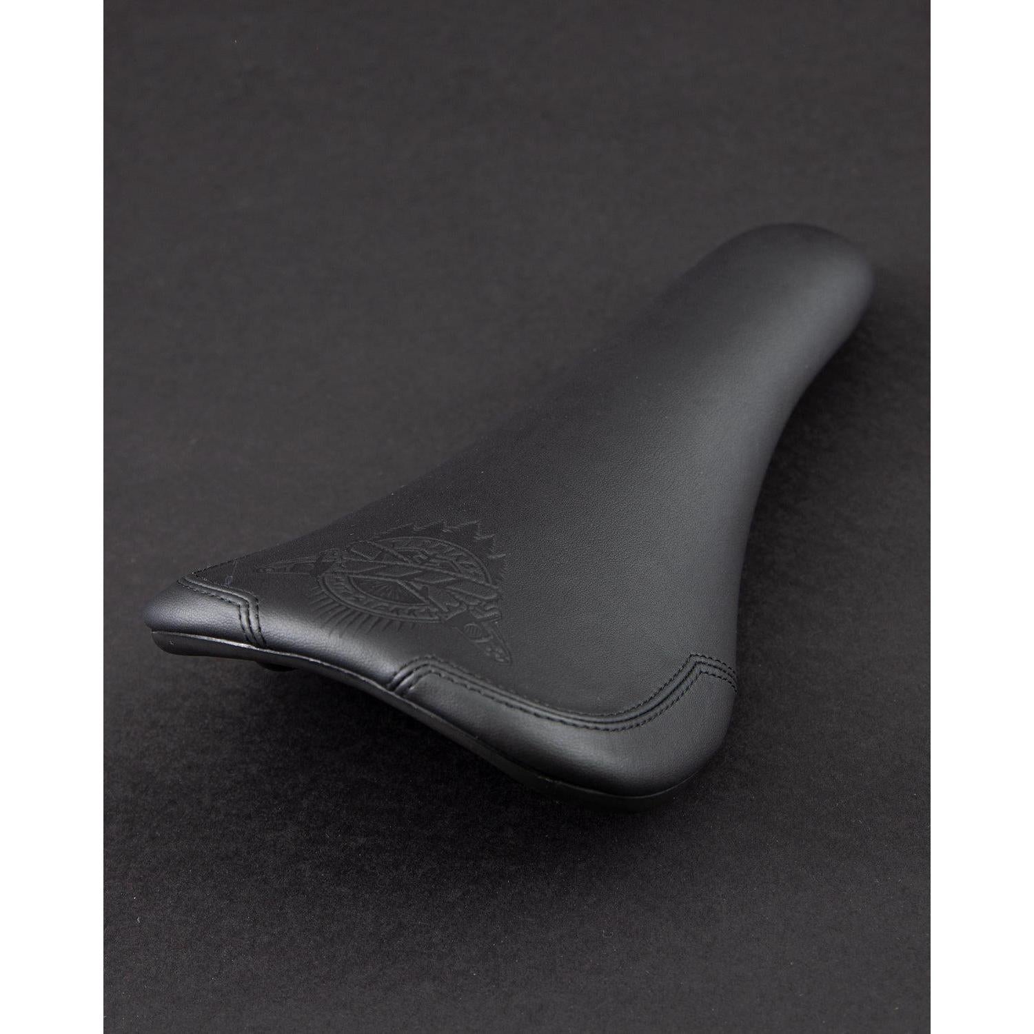 The Motosierra Railed Seat by Fly Bikes is a black seat with a textured logo on a dark background, made from synthetic leather and designed with a railed base for added stability.