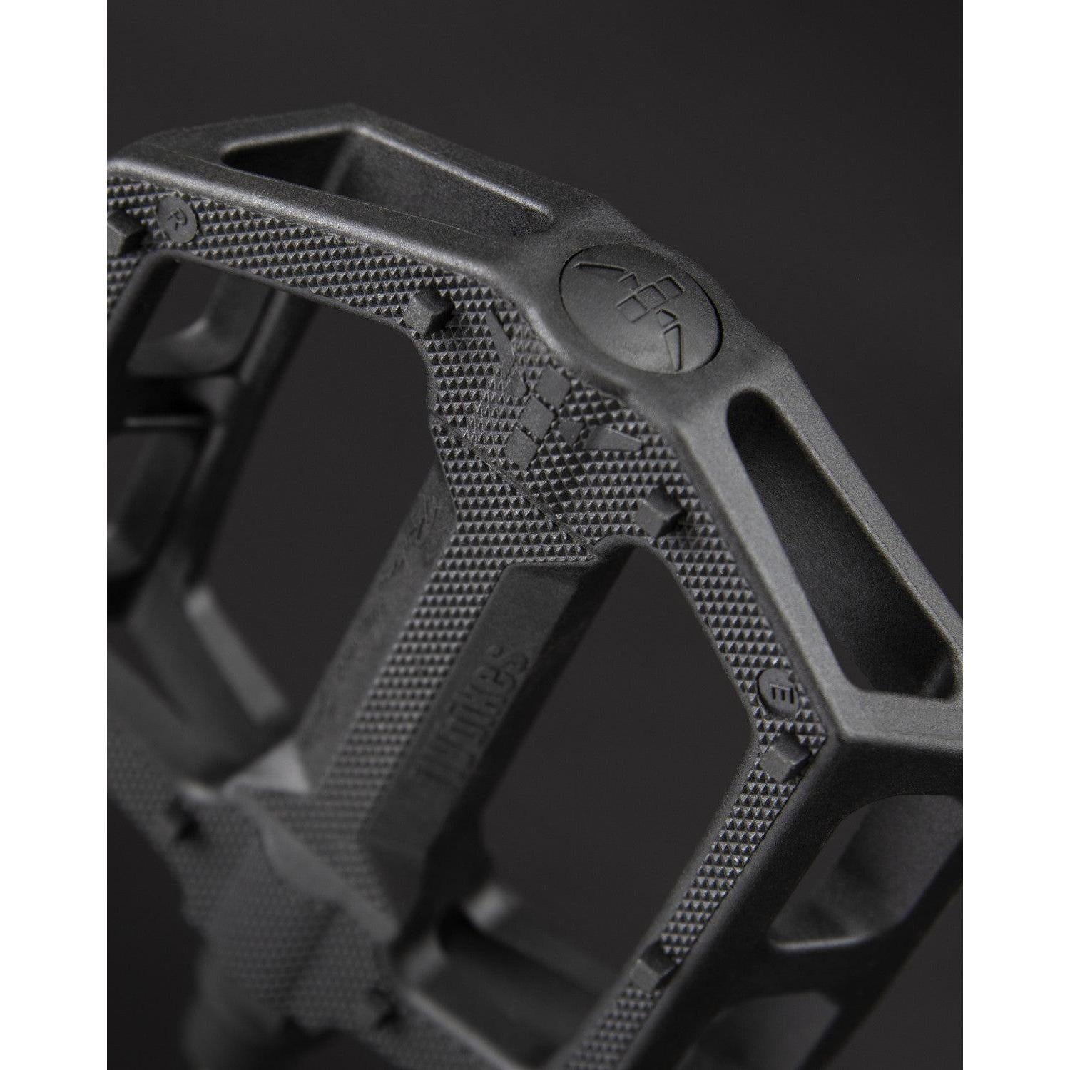 Close-up of Fly Bikes Ruben Pedals (Graphite), showcasing a durable black nylon fiberglass build, textured surface, geometric design, and robust chromoly axle against a dark backdrop.