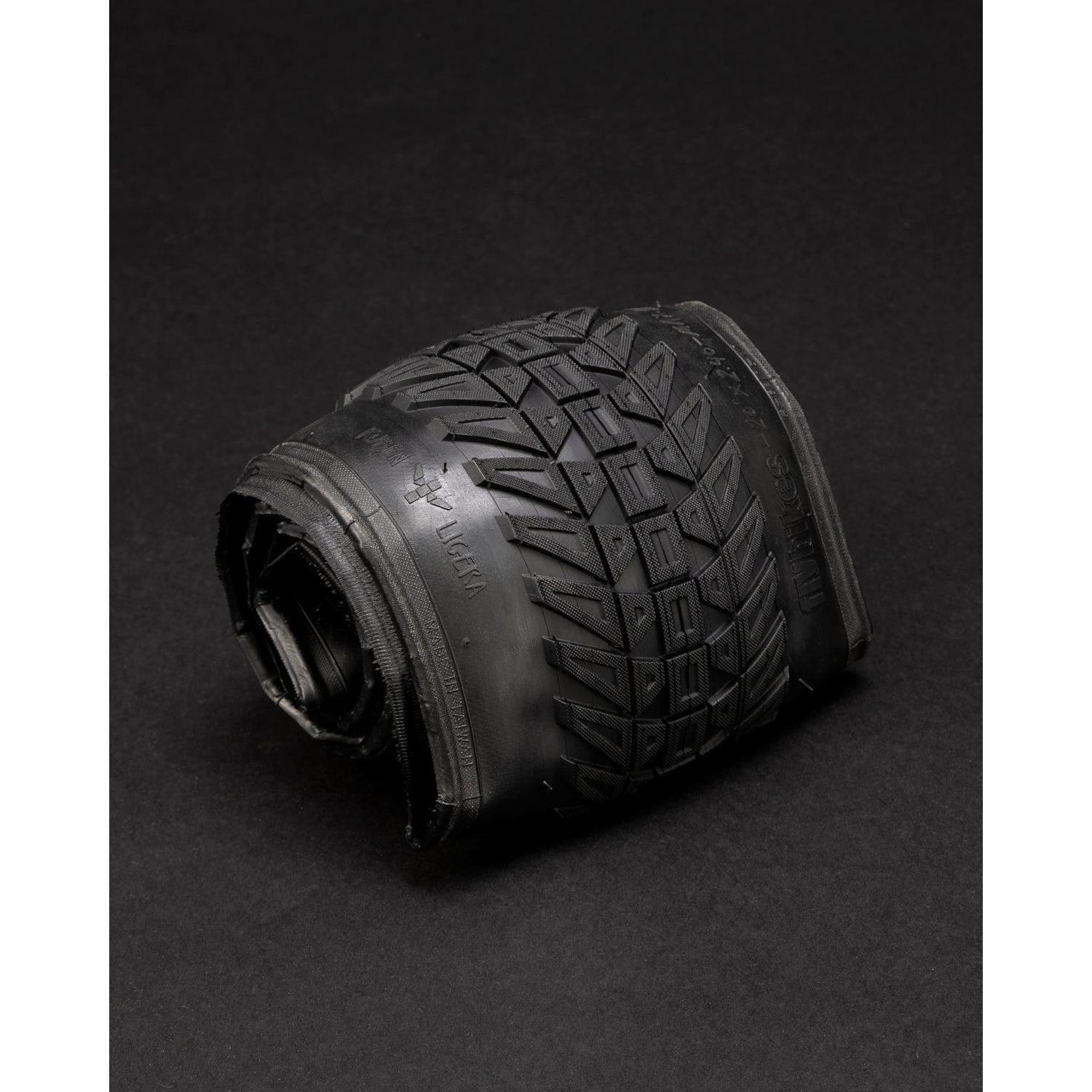 The Fly Bikes Ruben Tyre Ligera (Foldable) is a rolled-up black rubber car tire with Kevlar folding construction and visible tread pattern, elegantly showcased on a dark surface.