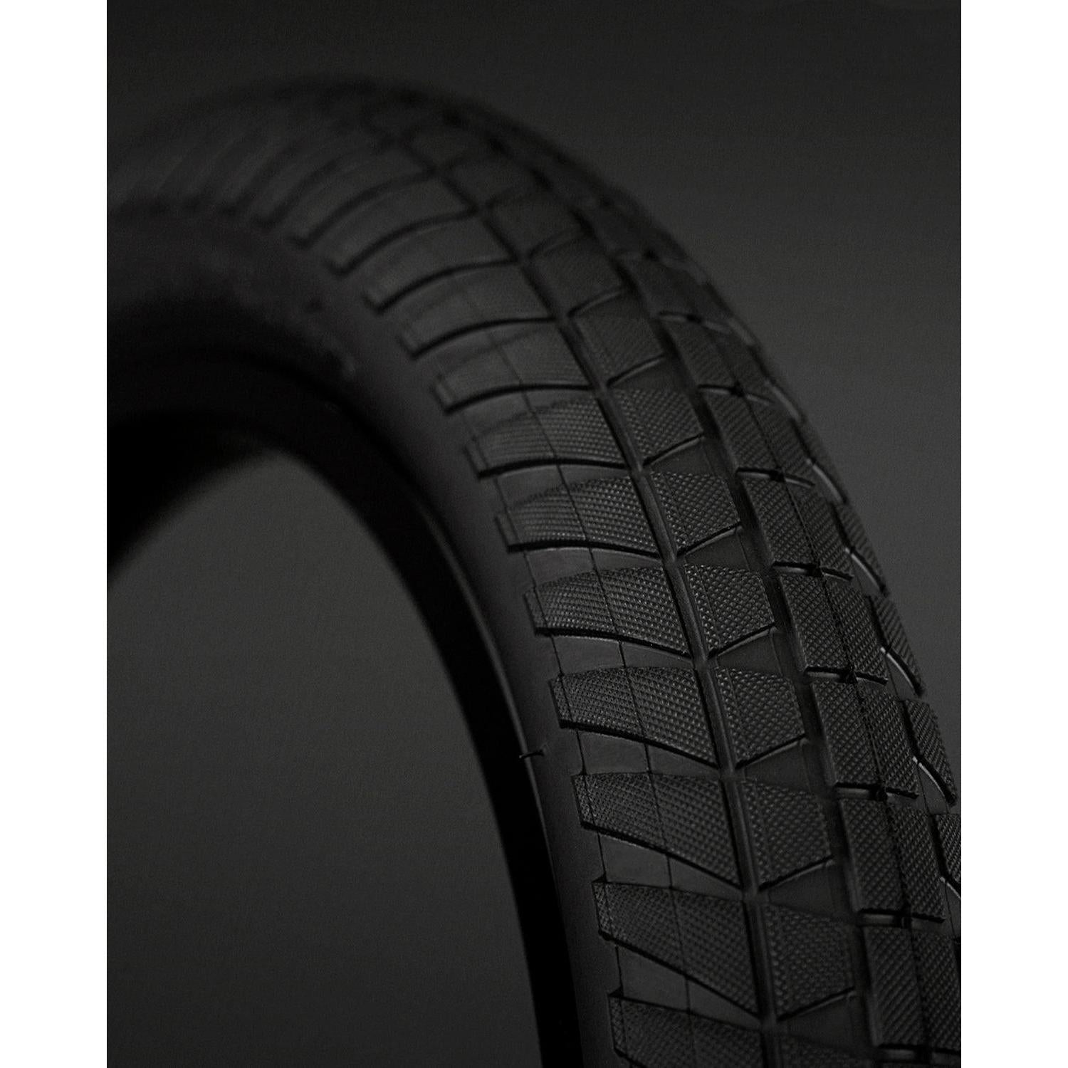 Close-up of a Fly Bikes Ruben Tyre STD bicycle tire with a textured tread pattern against a dark background, featuring 110 PSI and puncture-resistant technology for ultimate performance.
