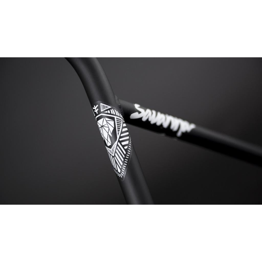 Close-up of Fly Bikes Savanna Bars featuring a black bicycle frame with a geometric white pattern and "scanner" in white text. The sleek design is enhanced by 4130 CrMo tubing, boosting strength and style.