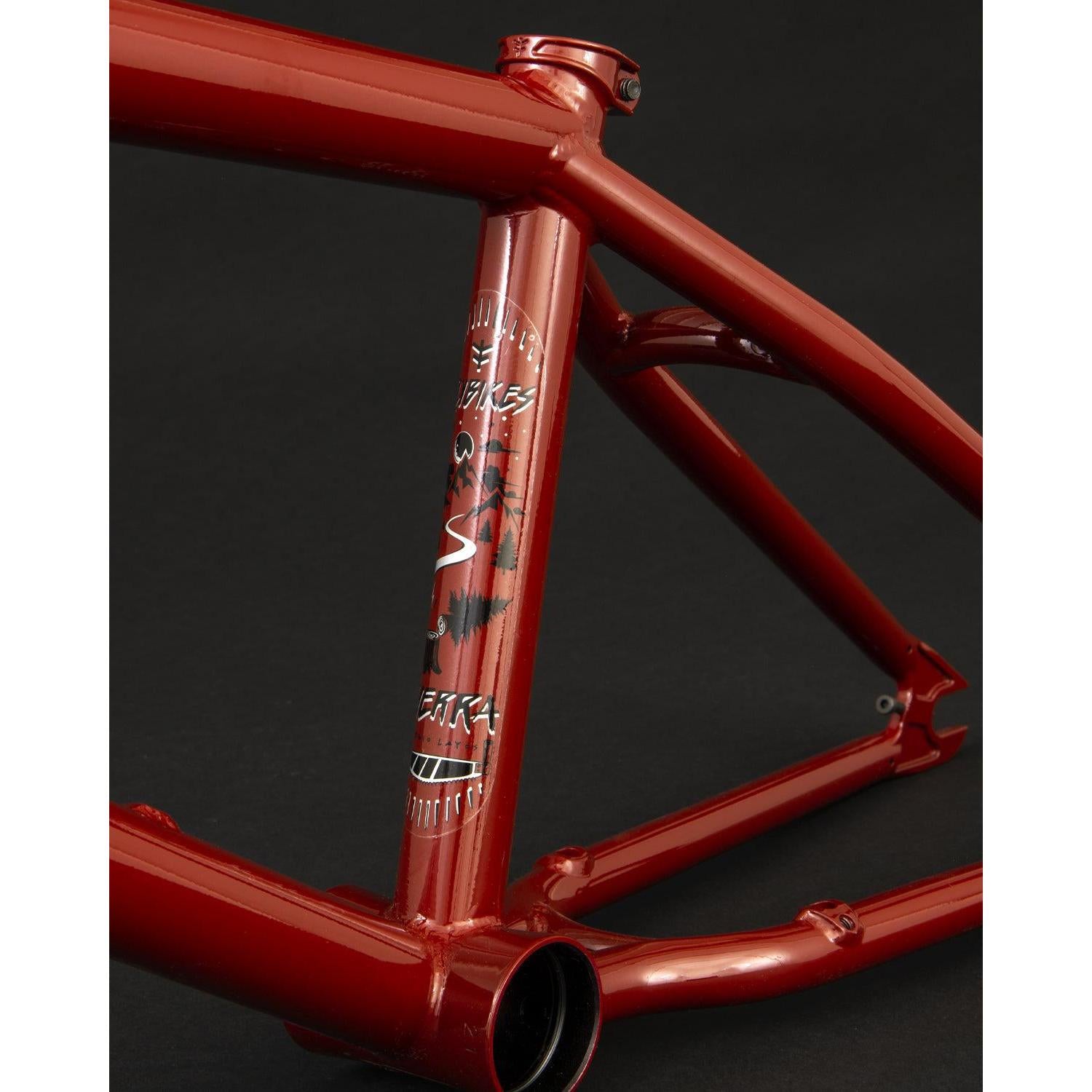 Close-up of a red Fly Bikes Sierra frame crafted from durable 4130 CrMo with a matte finish, featuring tree decals and "USA" on the vertical tube, against a black background.