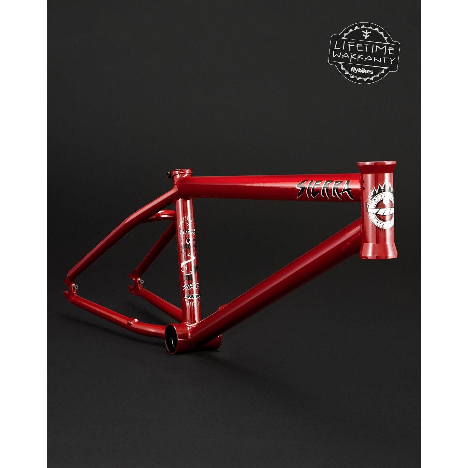 Fly Bikes Sierra Frame in red features a 4130 CrMo build with white graphics, a "Lifetime Warranty" badge on the top right, and Investment Cast components for enhanced durability against the stark black background.