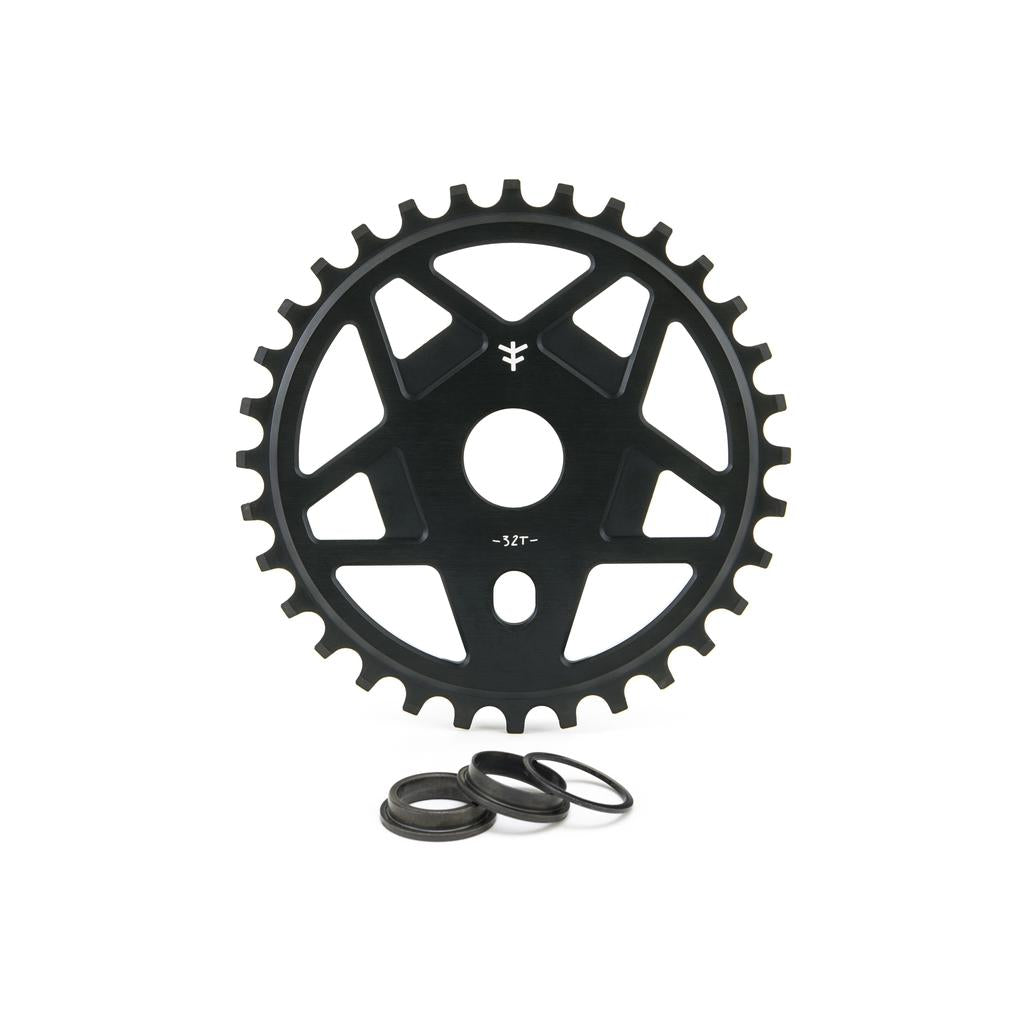 The Fly Bikes Tractor TT Sprocket is a sleek black gear made of 6061 T-6 Aluminum, designed with a central hole and edge teeth, accompanied by three circular washers for display.