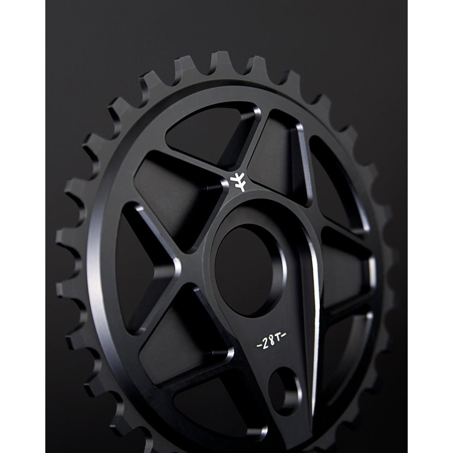 Close-up of the Fly Bikes Tractor XL Sprocket, a black bicycle chainring with 28 teeth, CNC machined from durable 6061 Aluminum, featuring geometric cutouts against a dark background.