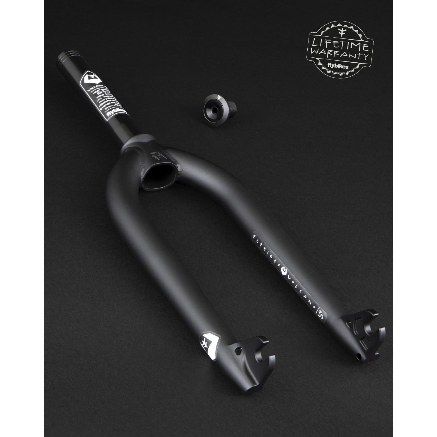 The Fly Bikes Volcano Forks, ideal for BMX steer-tubes, are presented on a dark background with an added metallic part. The black fork includes an attached label and a "Lifetime Warranty" badge, highlighting its exceptional durability and tire clearance.