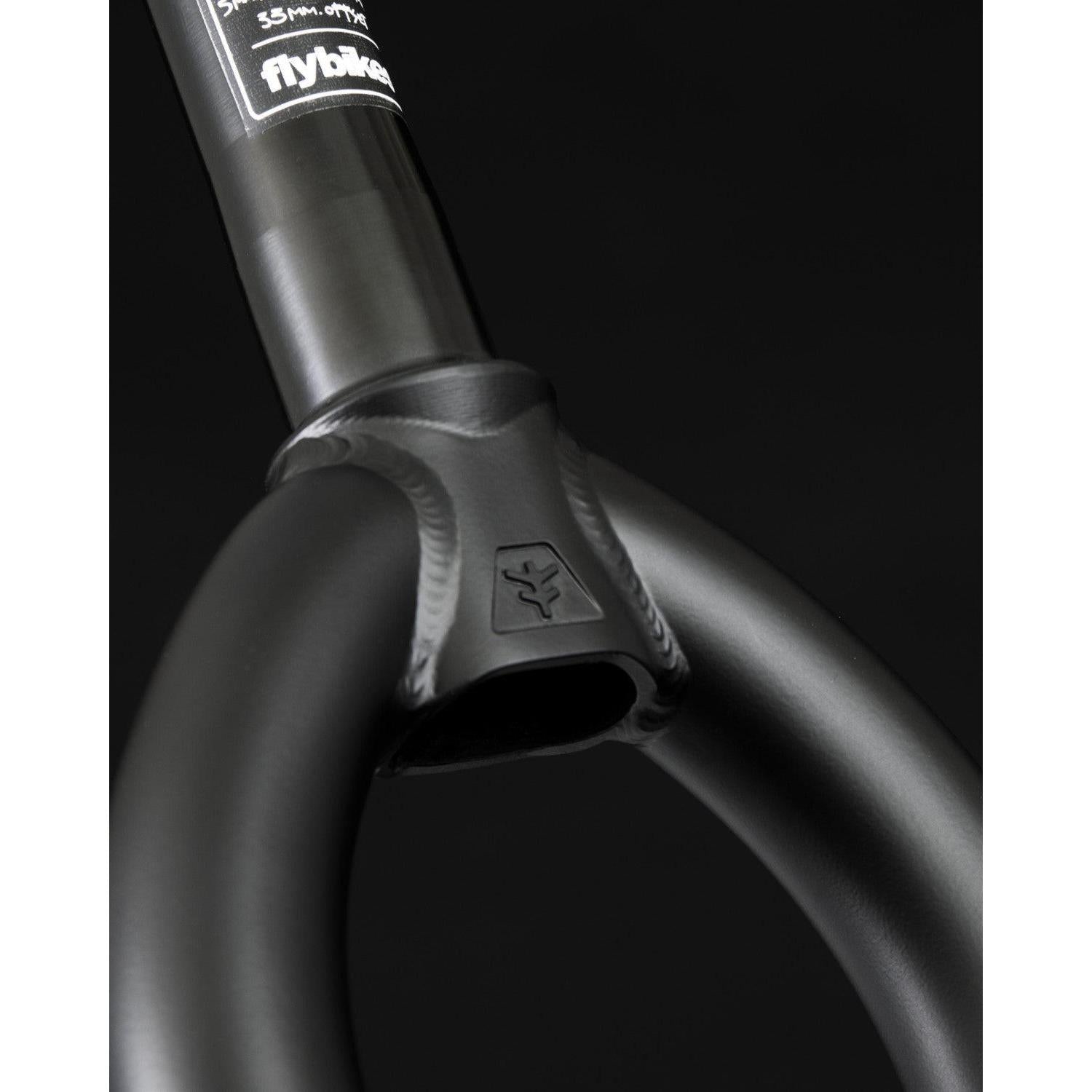 Close-up of Fly Bikes Volcano Forks in black, showcasing a logo, sticker, and matte finish. The BMX fork displays visible welds and excellent tire clearance for smooth rides.
