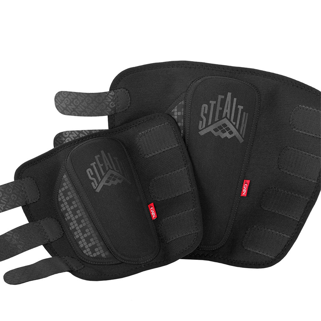 A pair of black protective pads with adjustable straps, showcasing the "STEALTH" brand logo. Made from DuraTec neoprene for comfort, these GAIN STEALTH Shin Guards also include KEVLAR material for increased durability and safety.