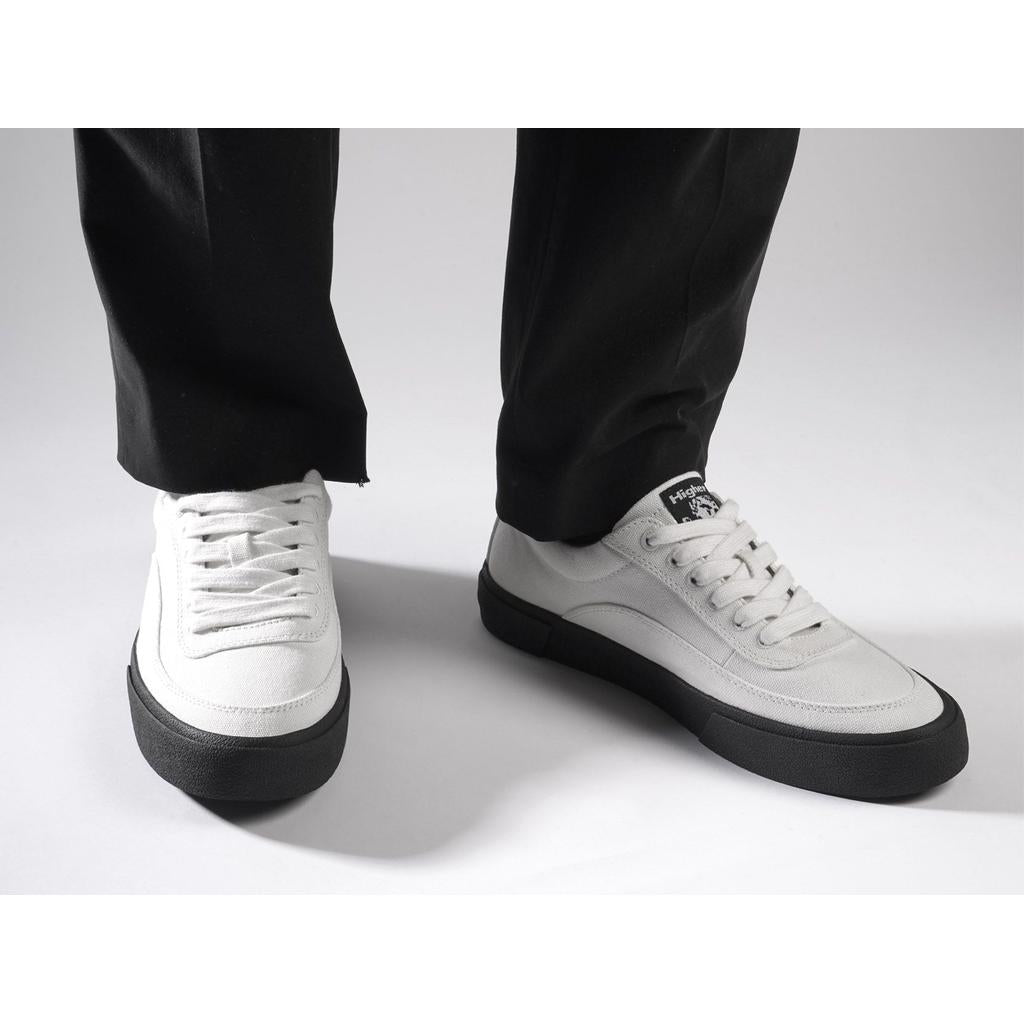 Person wearing Higher Crypt Canvas Lace Up Shoes (Raw Ecru/Black) with grippy black soles and black pants, standing on a light-colored surface.