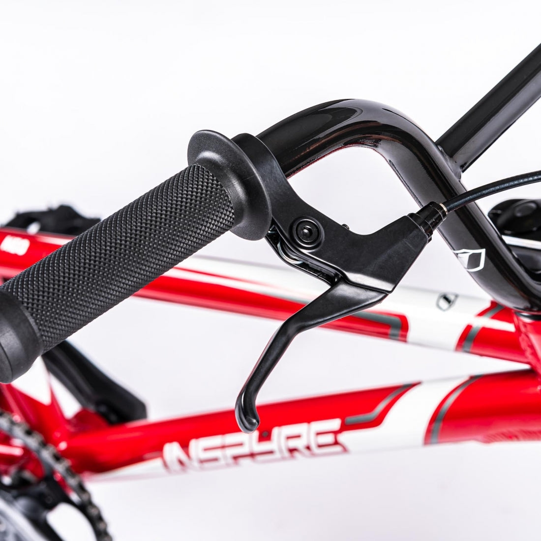Close-up of an Inspyre Neo Junior Bike's handlebar, brake lever, and gear shifter with a red and white frame in the background.