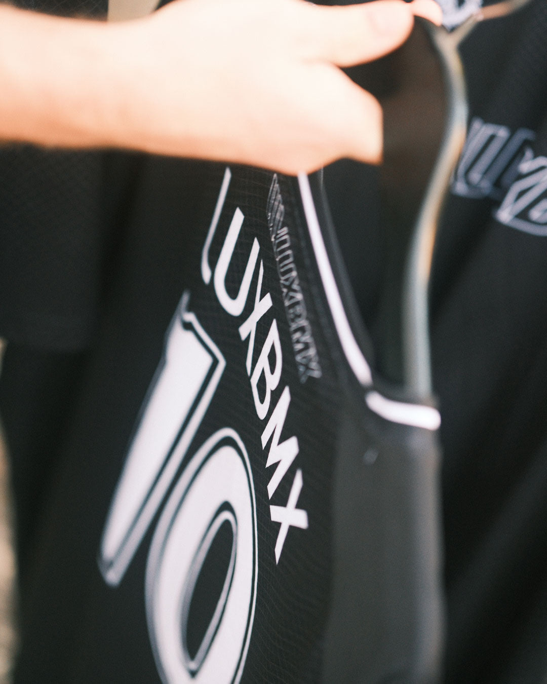 A person holds a black LUXBMX MMX Soccer Jersey - Custom Back Print on a hanger, highlighting its stylish look and breathable design perfect for BMX riders.