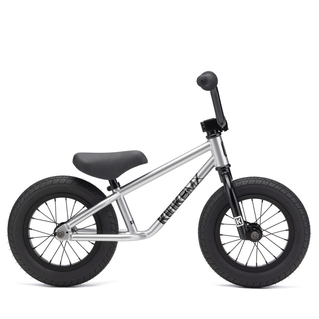 The Kink Coast 12 Inch Balance Bike features a minimalist silver frame with black saddle, grips, and tires. Designed like a pedal-free kids BMX, it's perfect for young children to improve balance while riding.