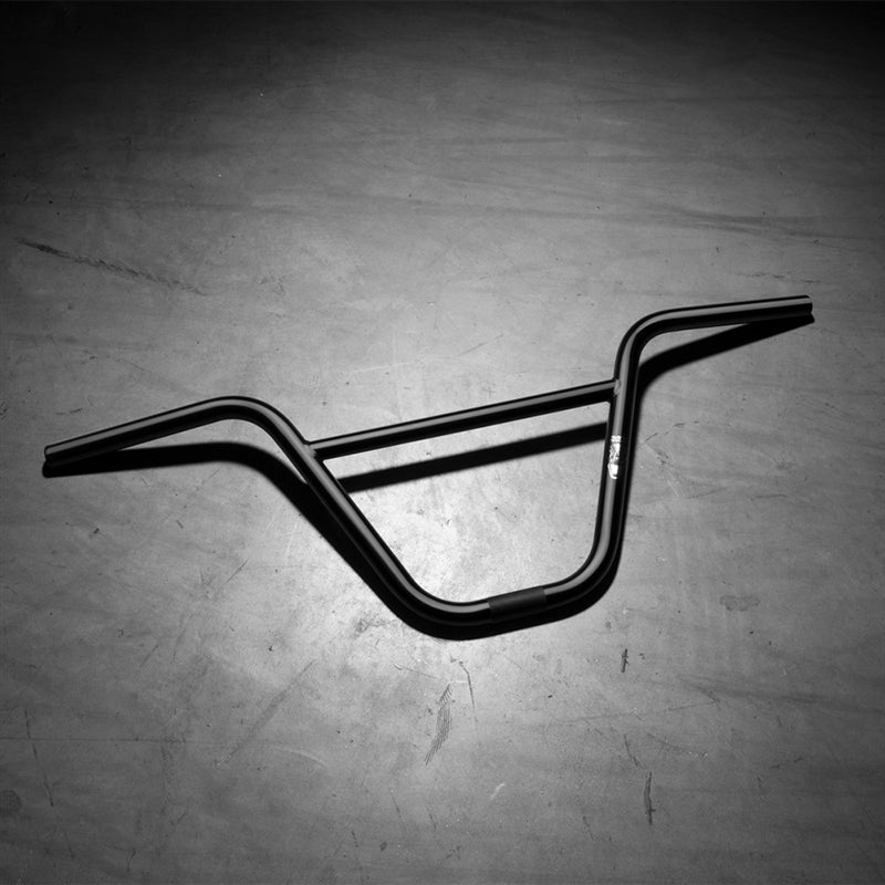 The Kink Rex Bar, a sleek BMX handlebar made from durable 4130 chromoly steel, rests on the concrete floor under glowing overhead lights.
