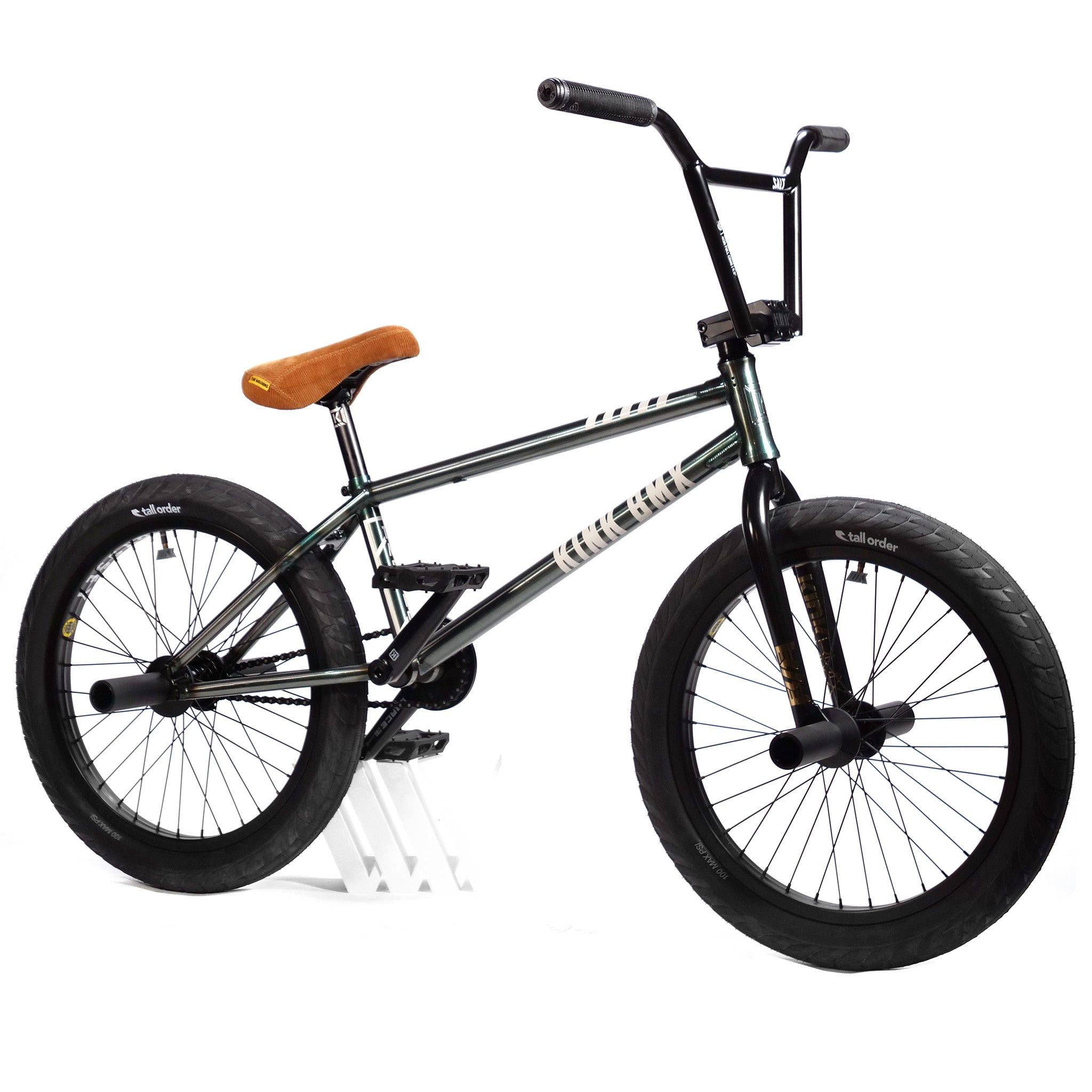 A budget-friendly custom build, the Kink Tactic Custom 20 Inch Bike boasts a sleek black frame, front and rear pegs on both wheels, black handlebars, and a brown saddle, all supported by a white stand.