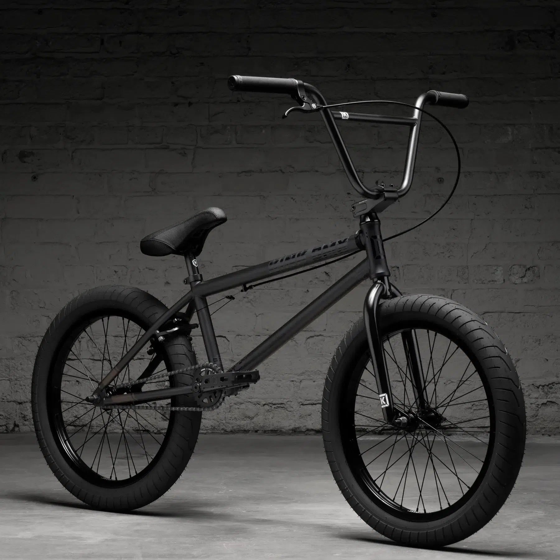 A Kink Whip 20 Inch BMX bike, model 2026, with a freecoaster hub and thick tires, is parked against a textured gray brick wall.