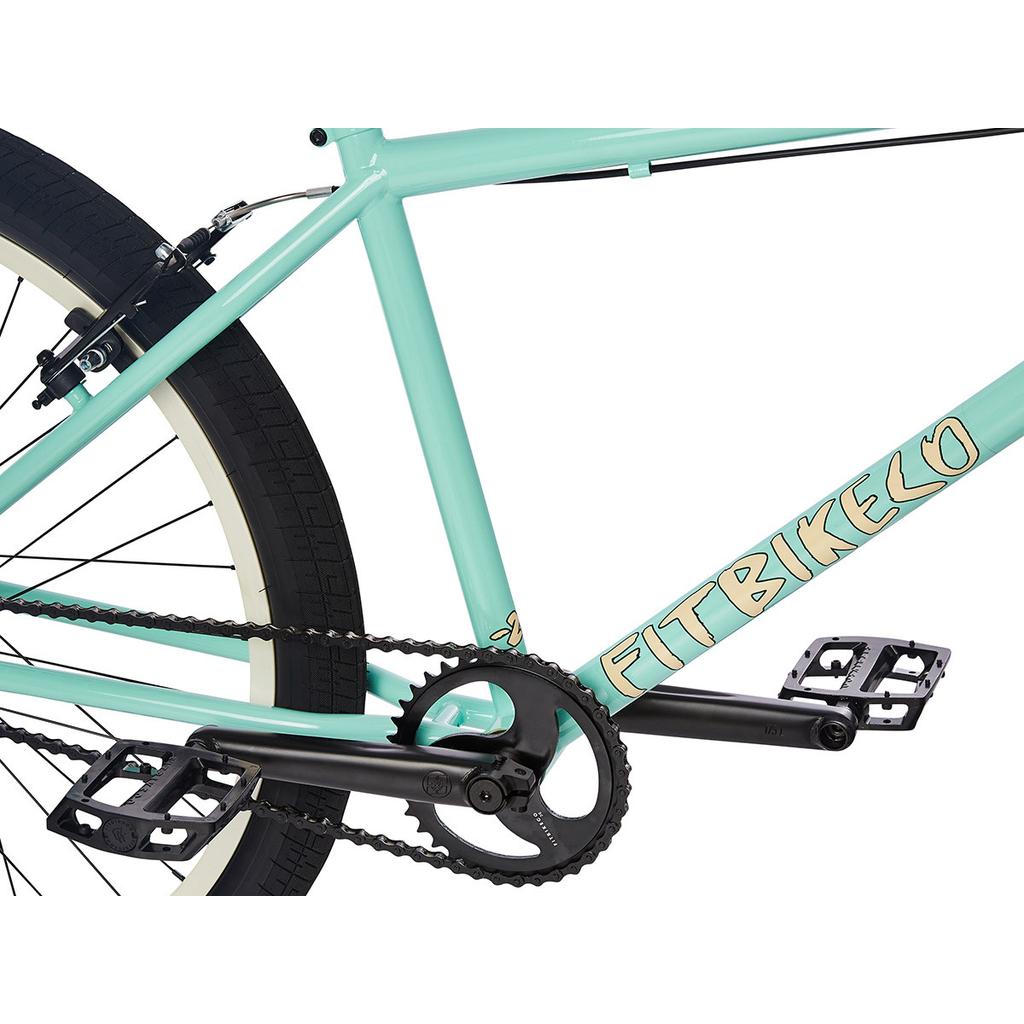 Close-up side view of the Fit CR26 Inch Bike’s mint green cr-mo frame, showing black pedals, crankset, chain, part of the rear tire, and visible "FIT BIKE CO" branding.