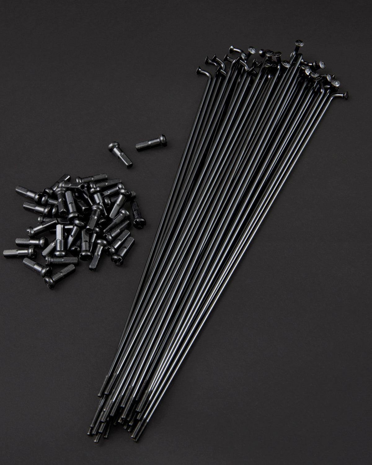 Fly Bikes Spokes (20 Pack) in black and stainless steel nipples are displayed on a dark surface, highlighting the precision of high-tension lacing.