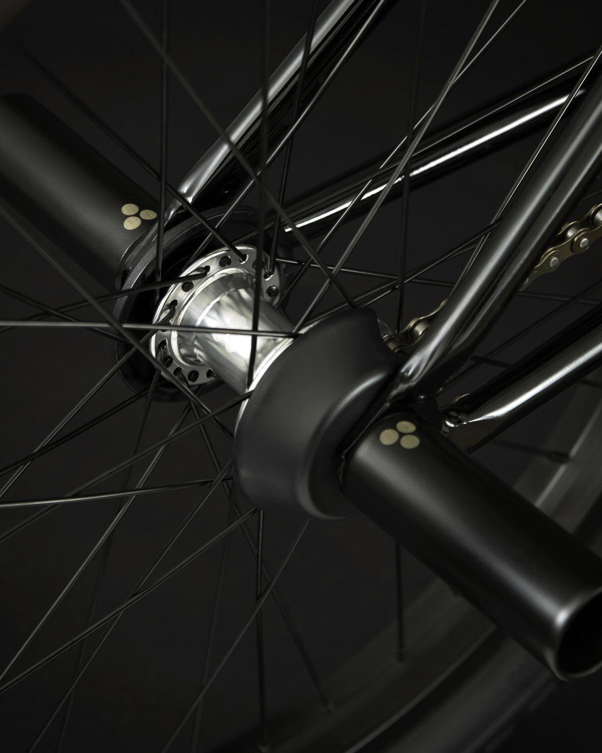 Close-up of the Fly Bikes Proton FC 20 Inch Bike's wheel, showcasing black spokes with a silver hub and black pegs on the axle. This durable configuration is complemented by its CrMo frame, providing a robust ride.