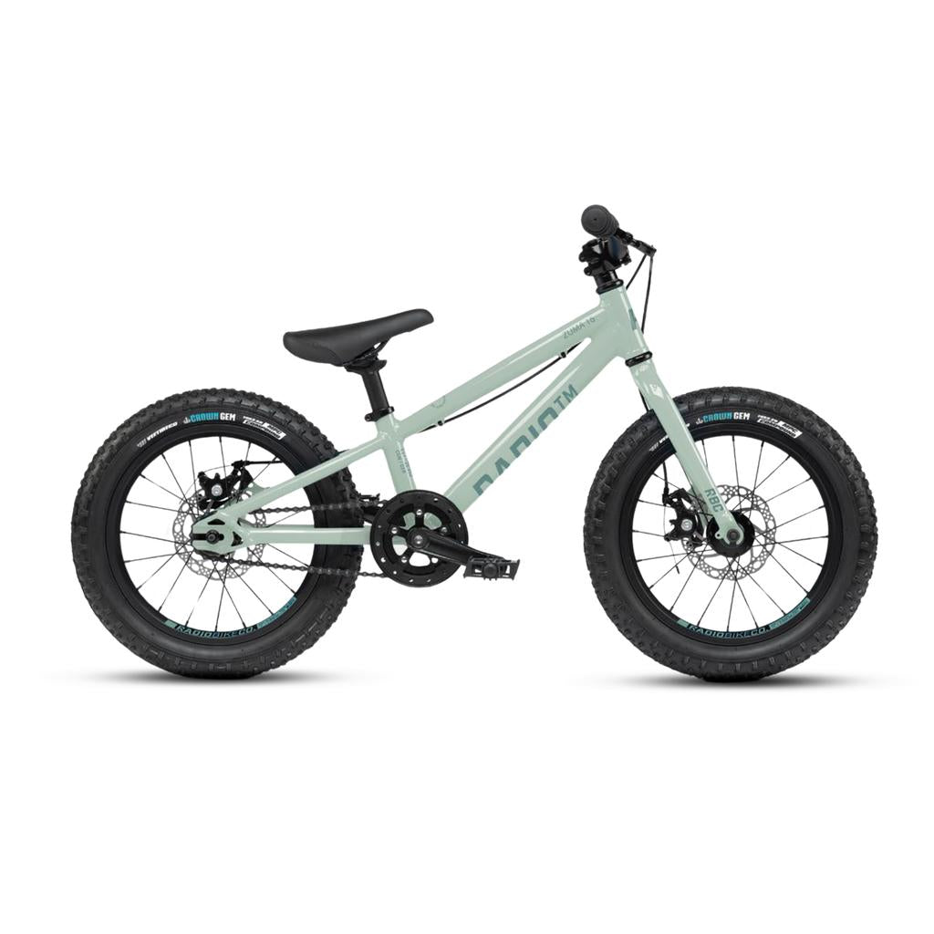 The Radio 16 Inch Zuma Bike is a lightweight kids' mountain bike with thick tires, disc brakes, flat handlebars, a black saddle, and a light gray frame, pictured from the side against a white background.
