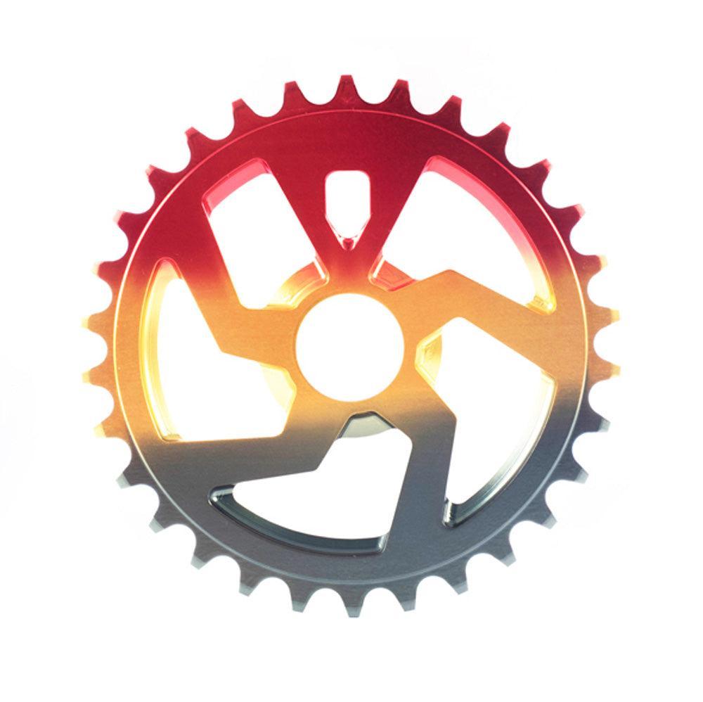 The Cult NWO Sprocket, a BMX chainring made from strong 7075-T6 aluminum with geometric cutouts, is displayed on a white background featuring a red and yellow gradient overlay.