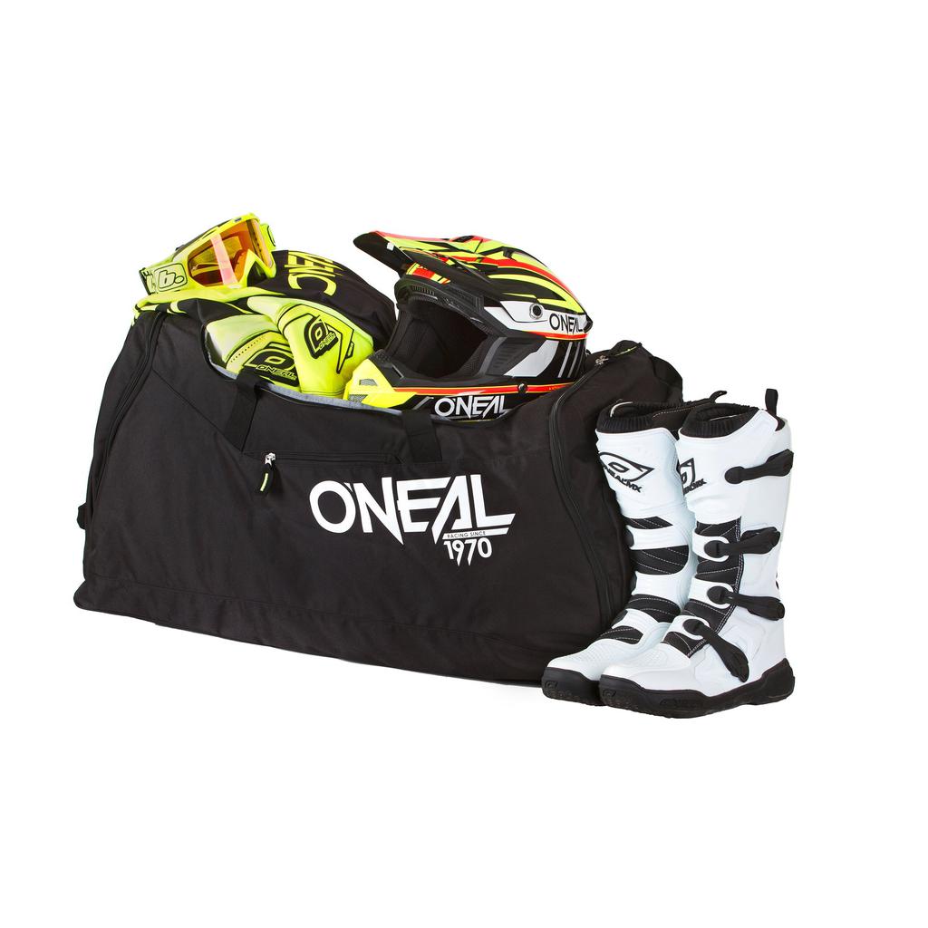 The Oneal TX800 Gear Bag in black, made from durable 600D polyester, holds a yellow and black motocross helmet and gloves. White motocross boots with black straps are placed neatly beside it.
