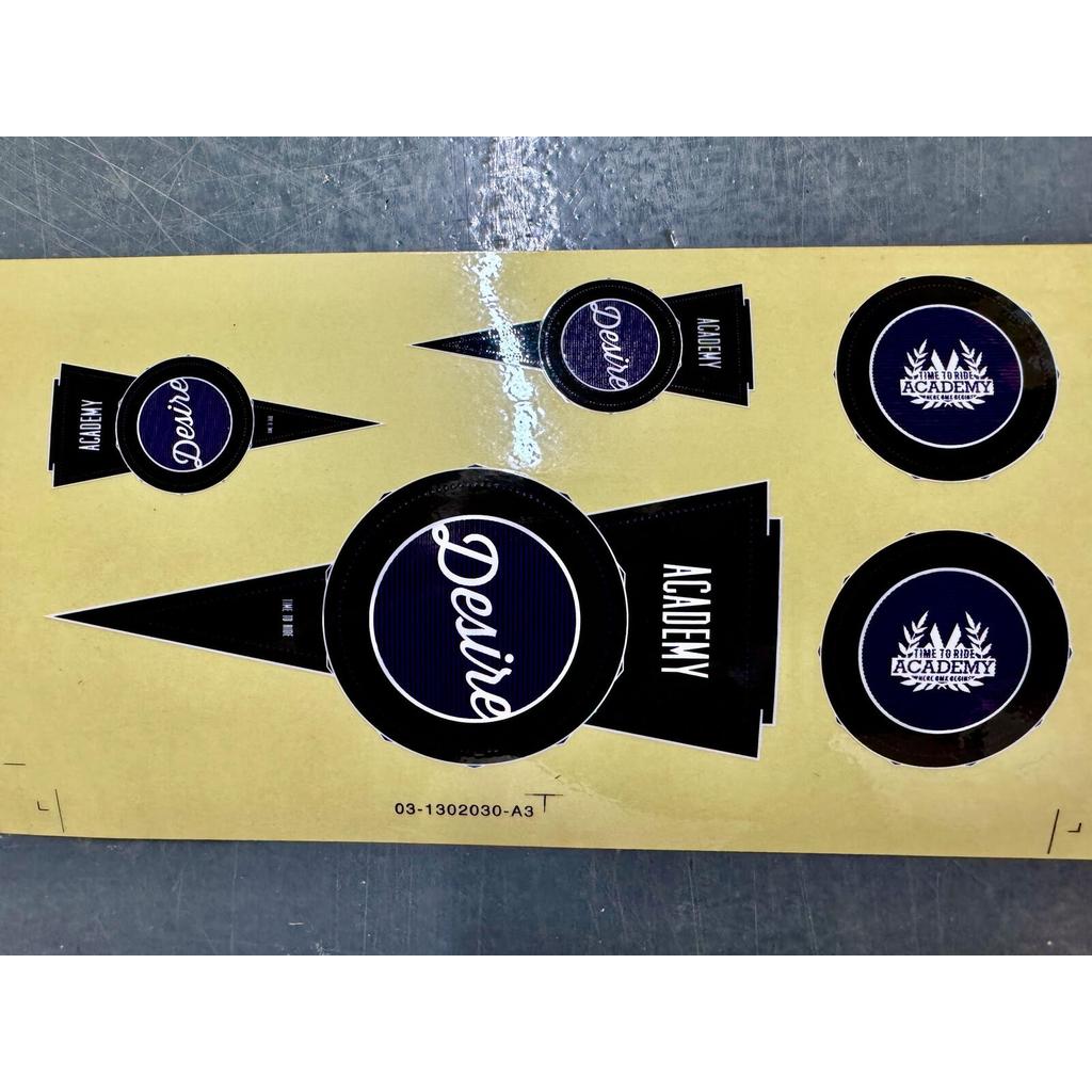 Academy Desire Sticker Pack featuring a sheet of 2017 purple and grey replacement stickers with circular logos and pennant-shaped designs inscribed with the text “Desire” and “Academy.”